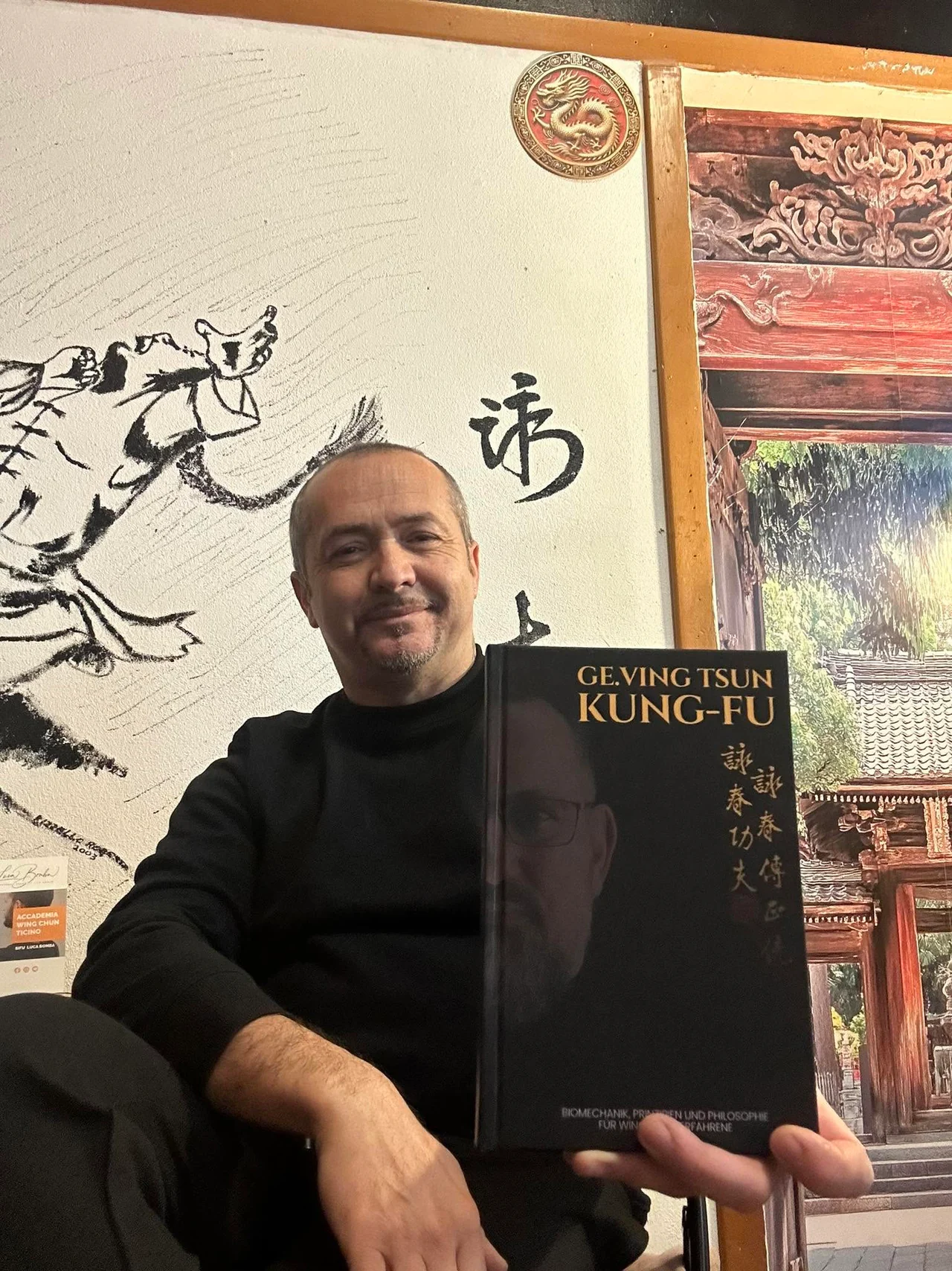 Sifu Luca Bomba nella sala, con il libro Ving Tsun Kung-Fu davanti al murale